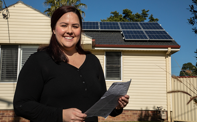 Woman with energy bill outside her home which has solar panels on the roof.
