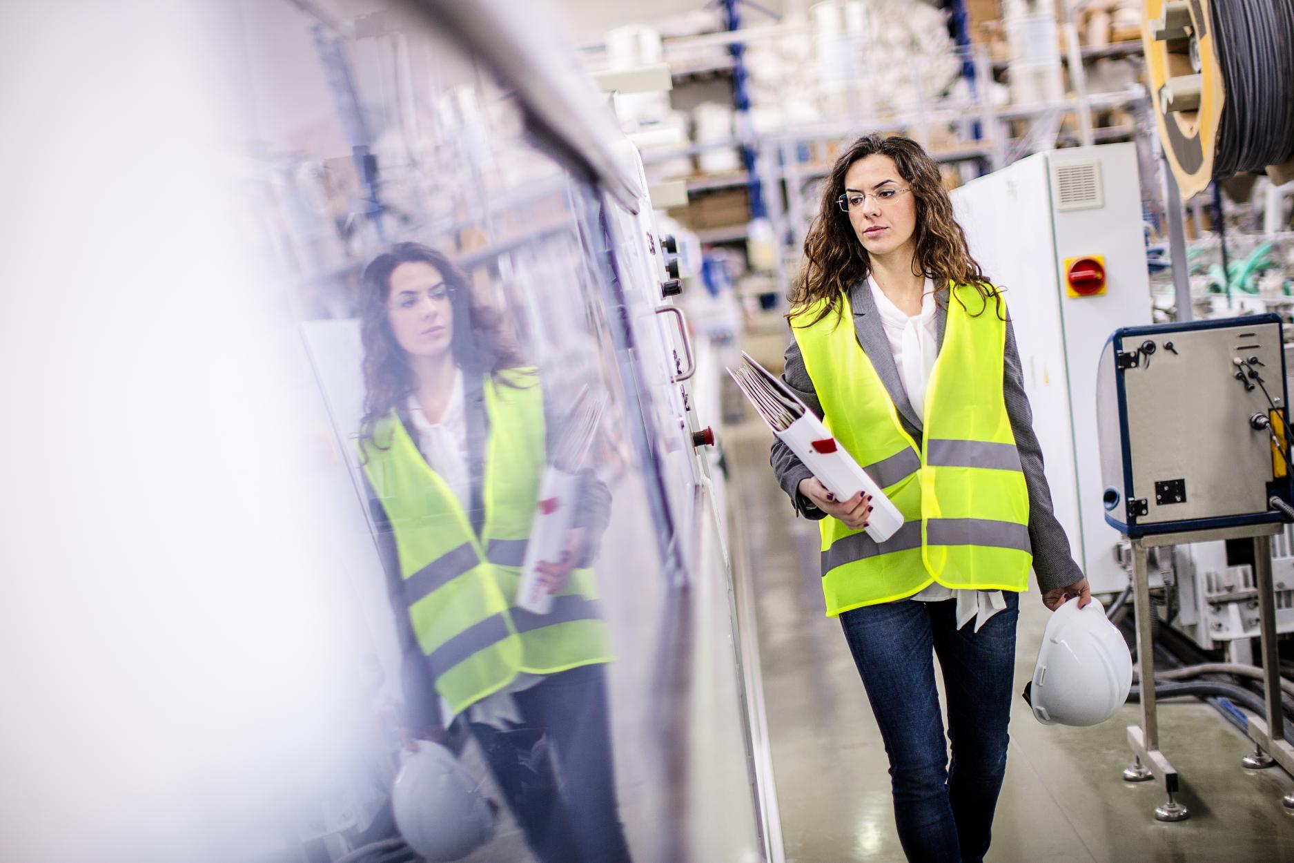 Female worker walking through factory holding hard hat