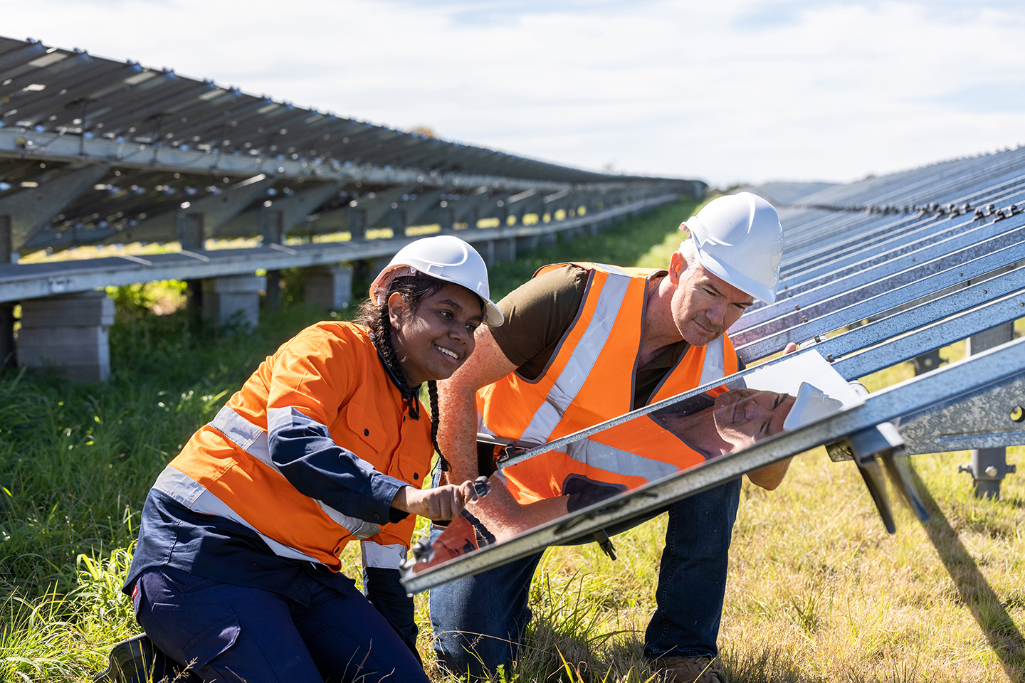 Woman and man kneeling in front of solar panels