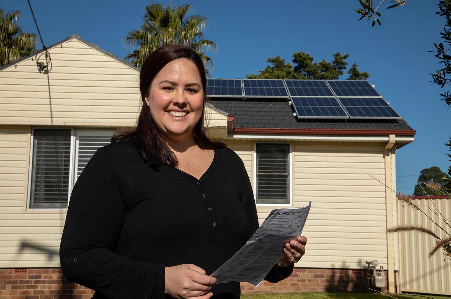 Solar program participant standing outside house with solar panels