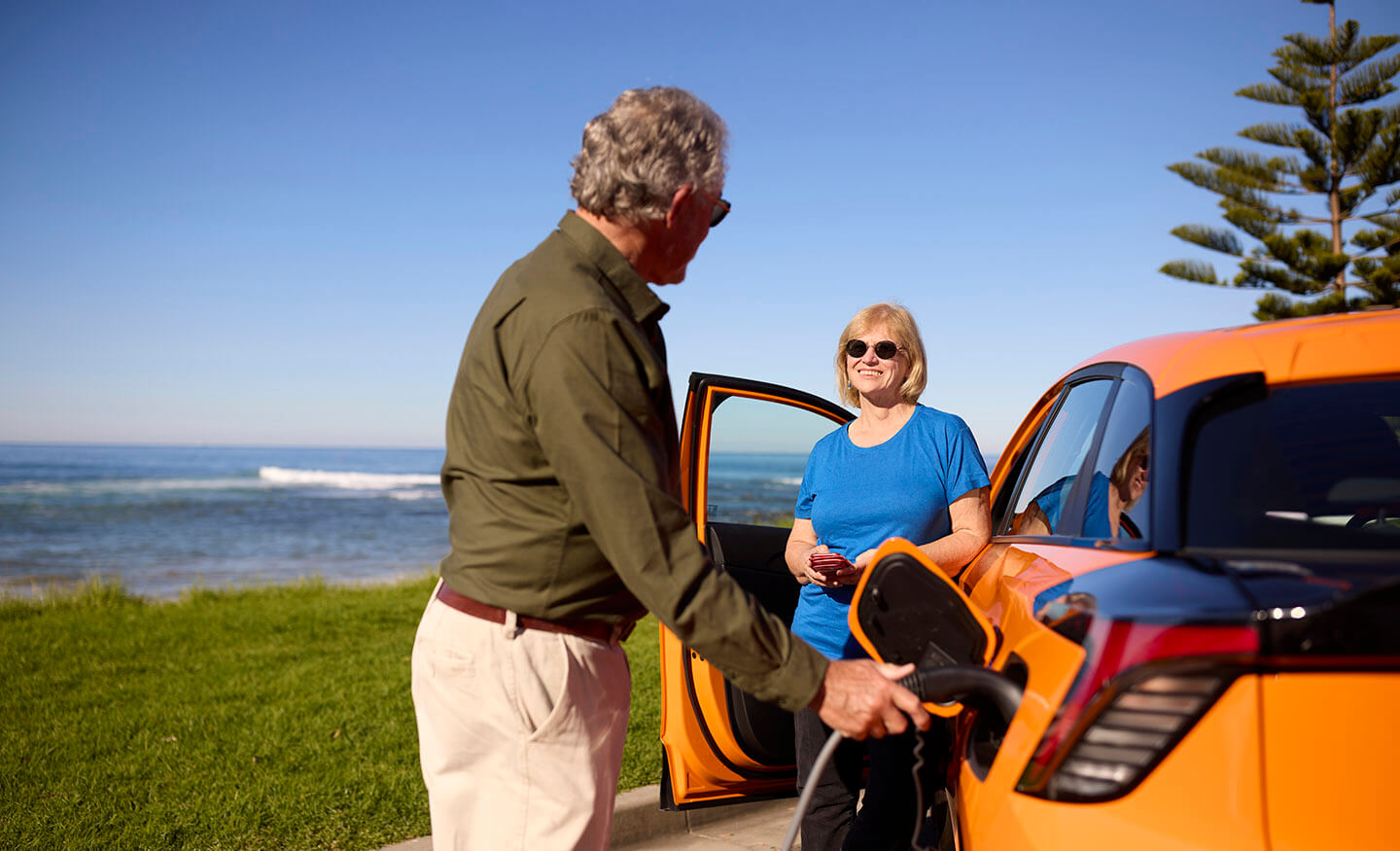 Two people charging electric vehicle near a beach