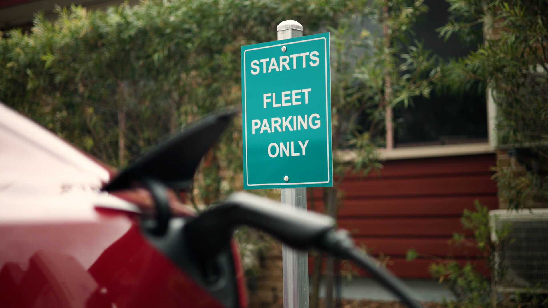 A street sign that reads STARTTS Fleet parking only, with a plugged in red electric vehicle in the bottom of the image.