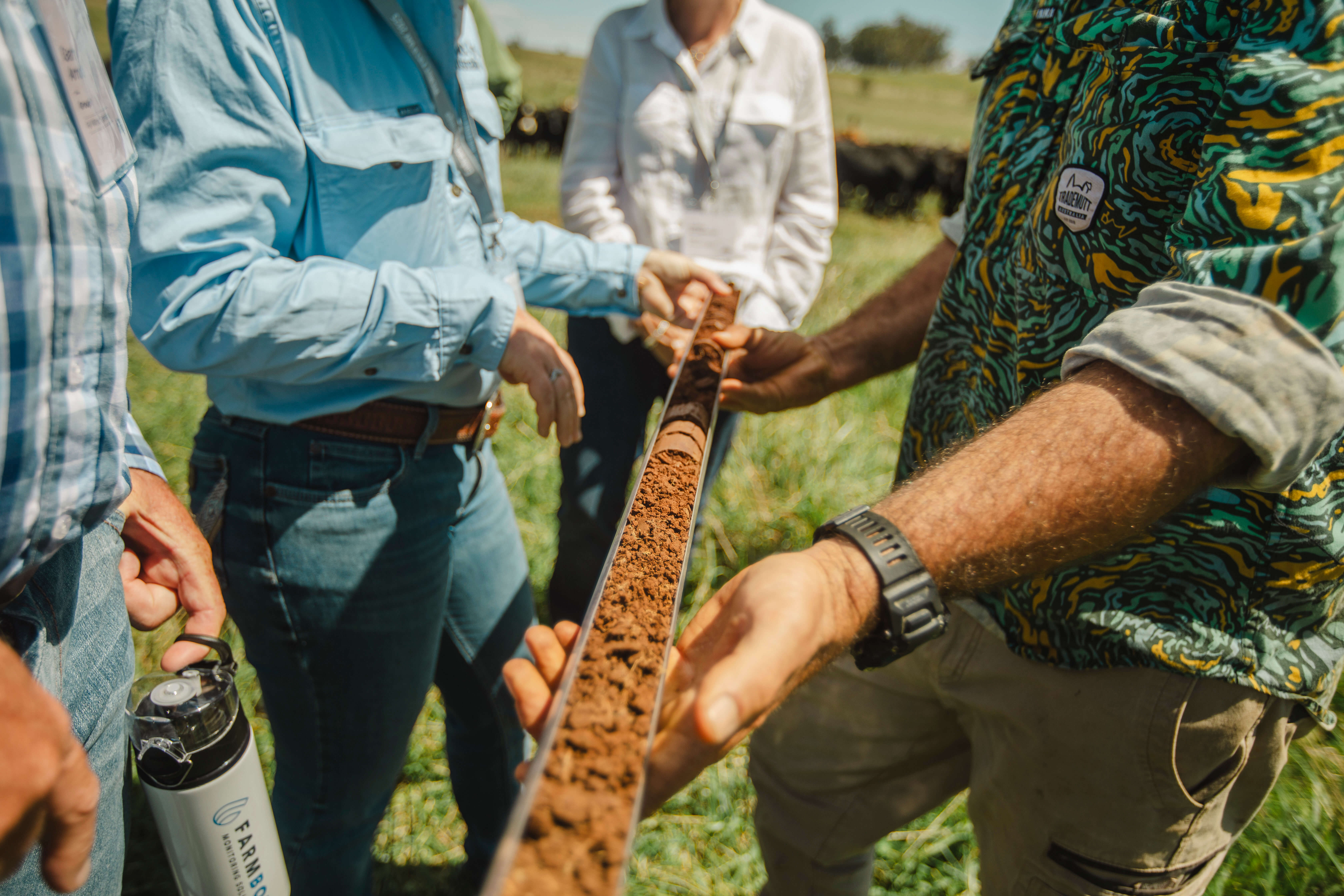 Farmers inspect a one metre soil core in a perspex holder that is mid-brown in coloured and crumbly in texture
