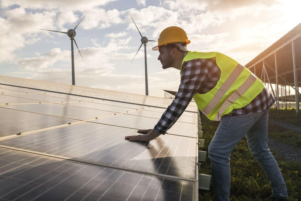 Worker in hat outdoors leaning on solar panel