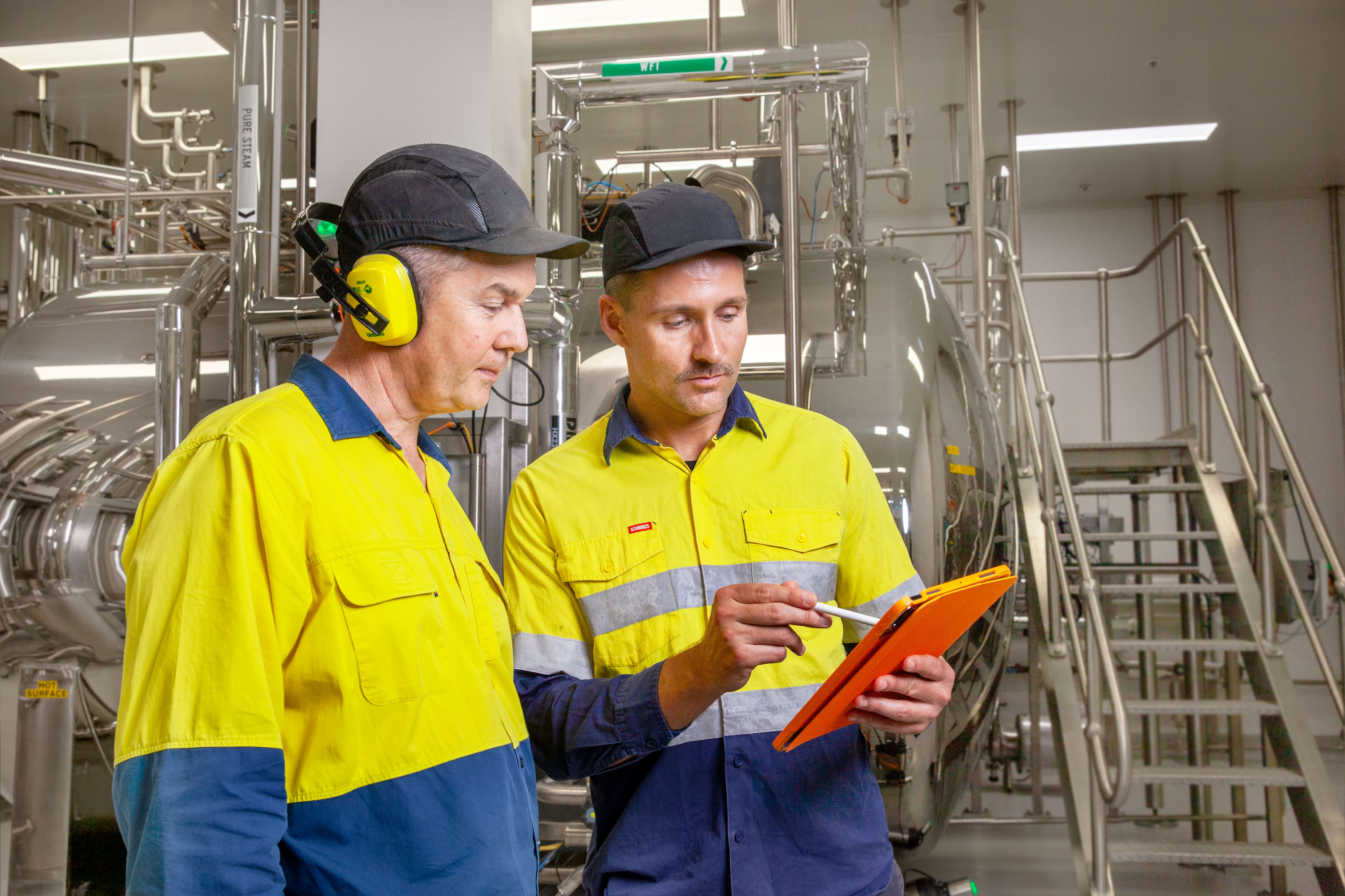 Two men in high visibility workwear standing in front of industrial boilers