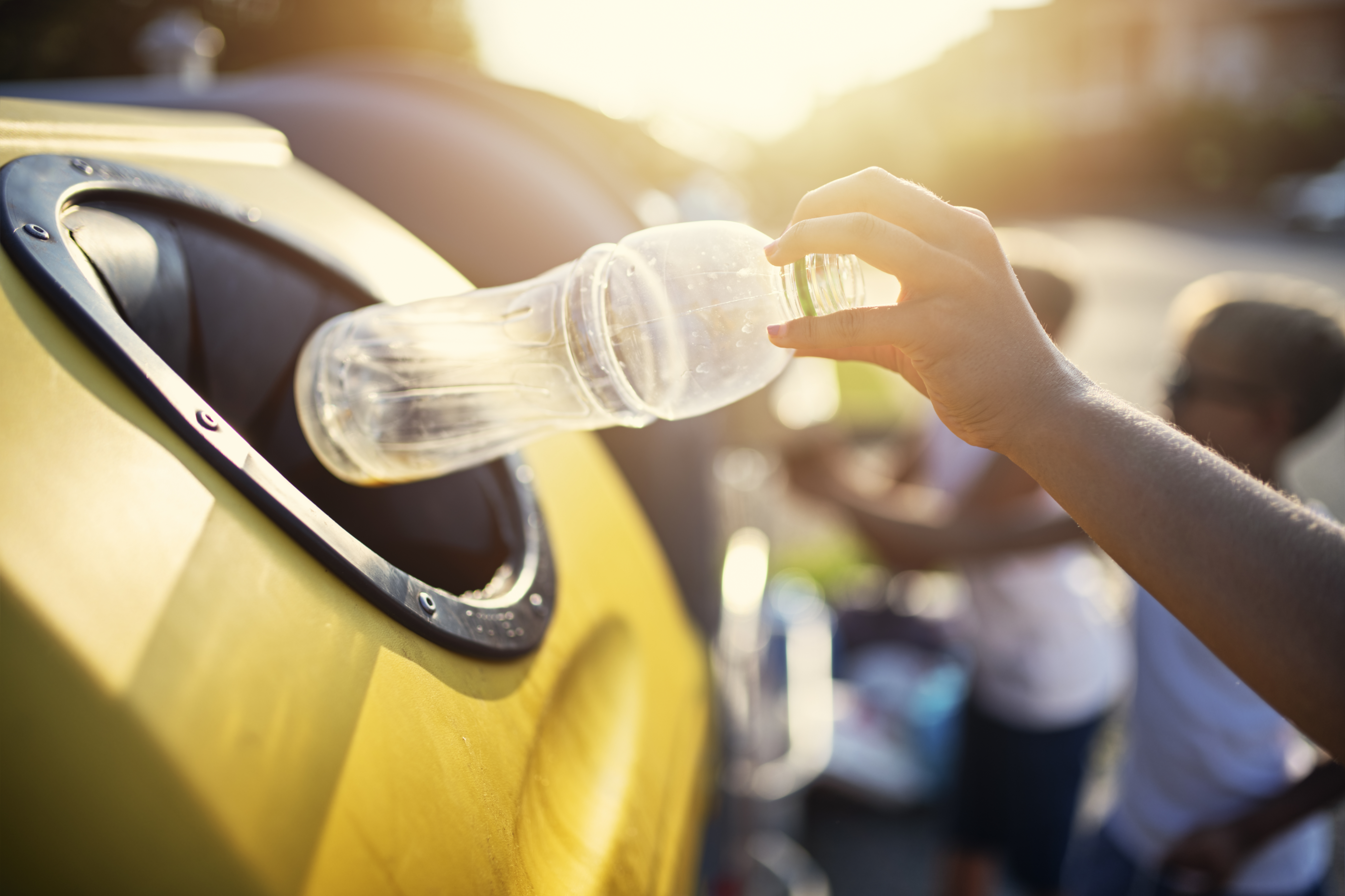 Person throwing a plastic bottle into a recycling bin