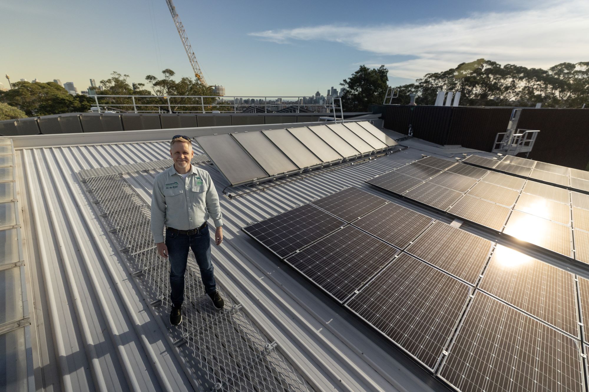 Jon wearing his zoo uniform standing on a roof surrounded by solar panels