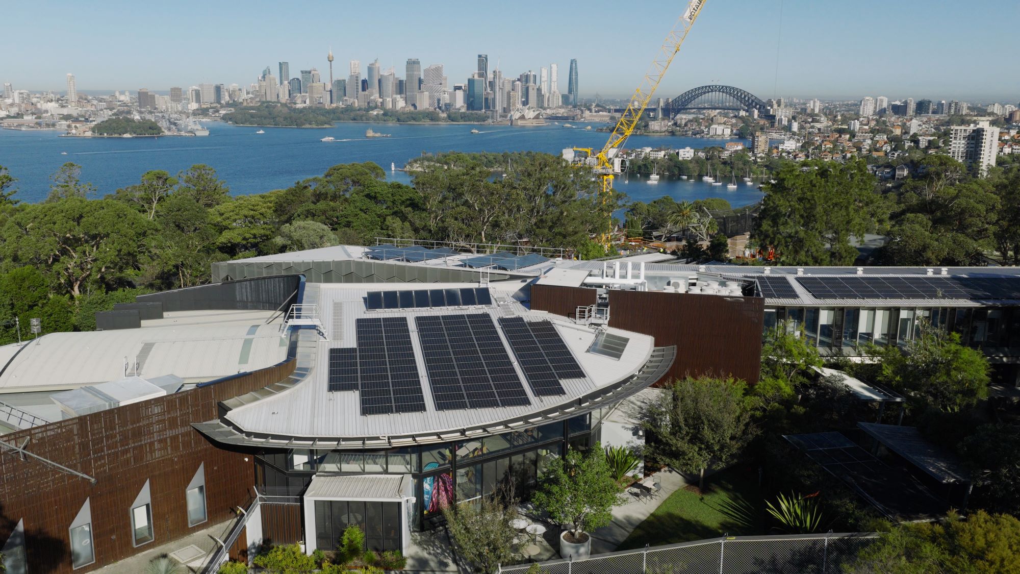 Aerial view of Taronga Zoo building with solar panels on the roof and the Sydney city skyline in the distance