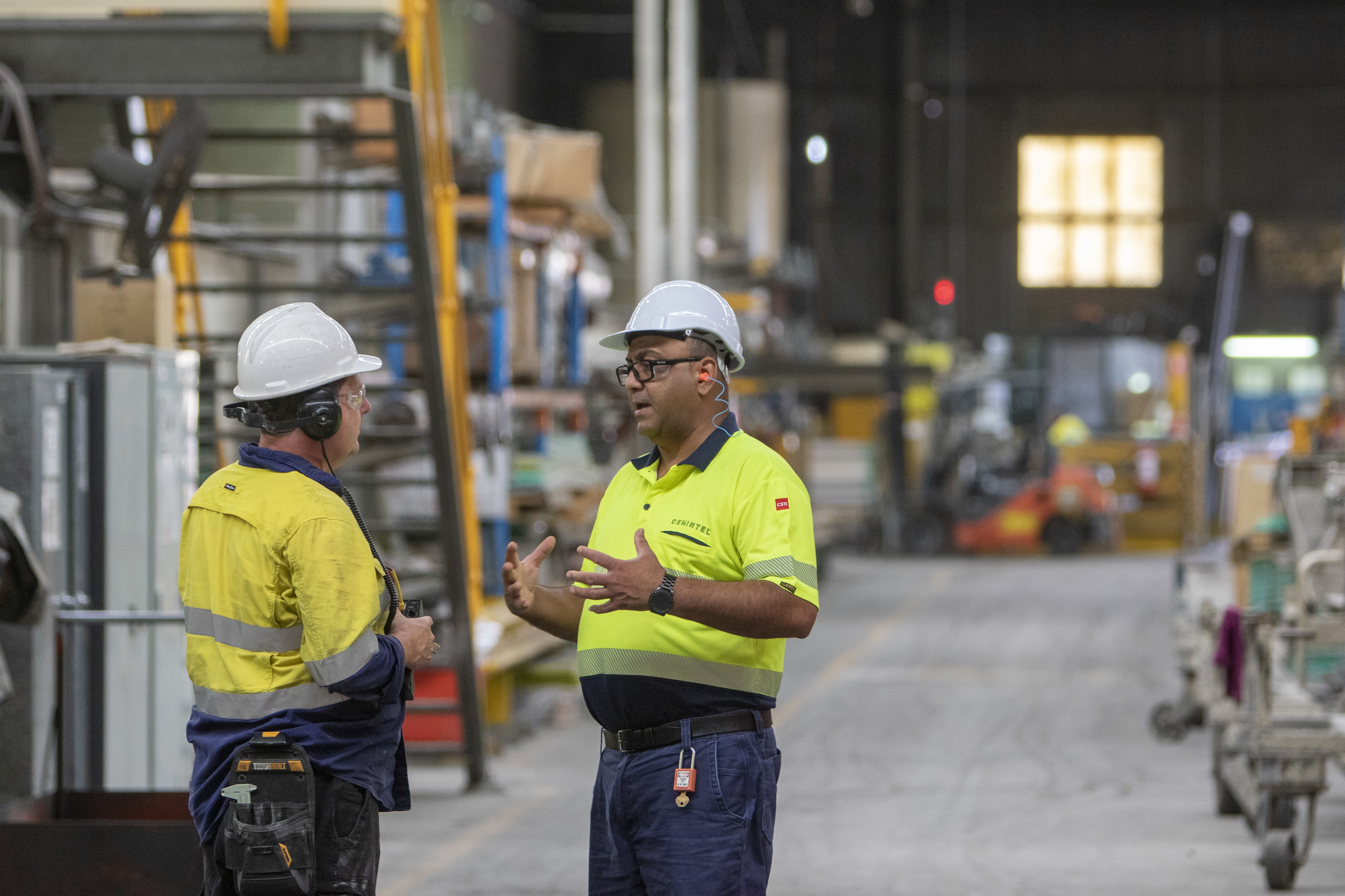 Two trades people talking inside a large factory warehouse