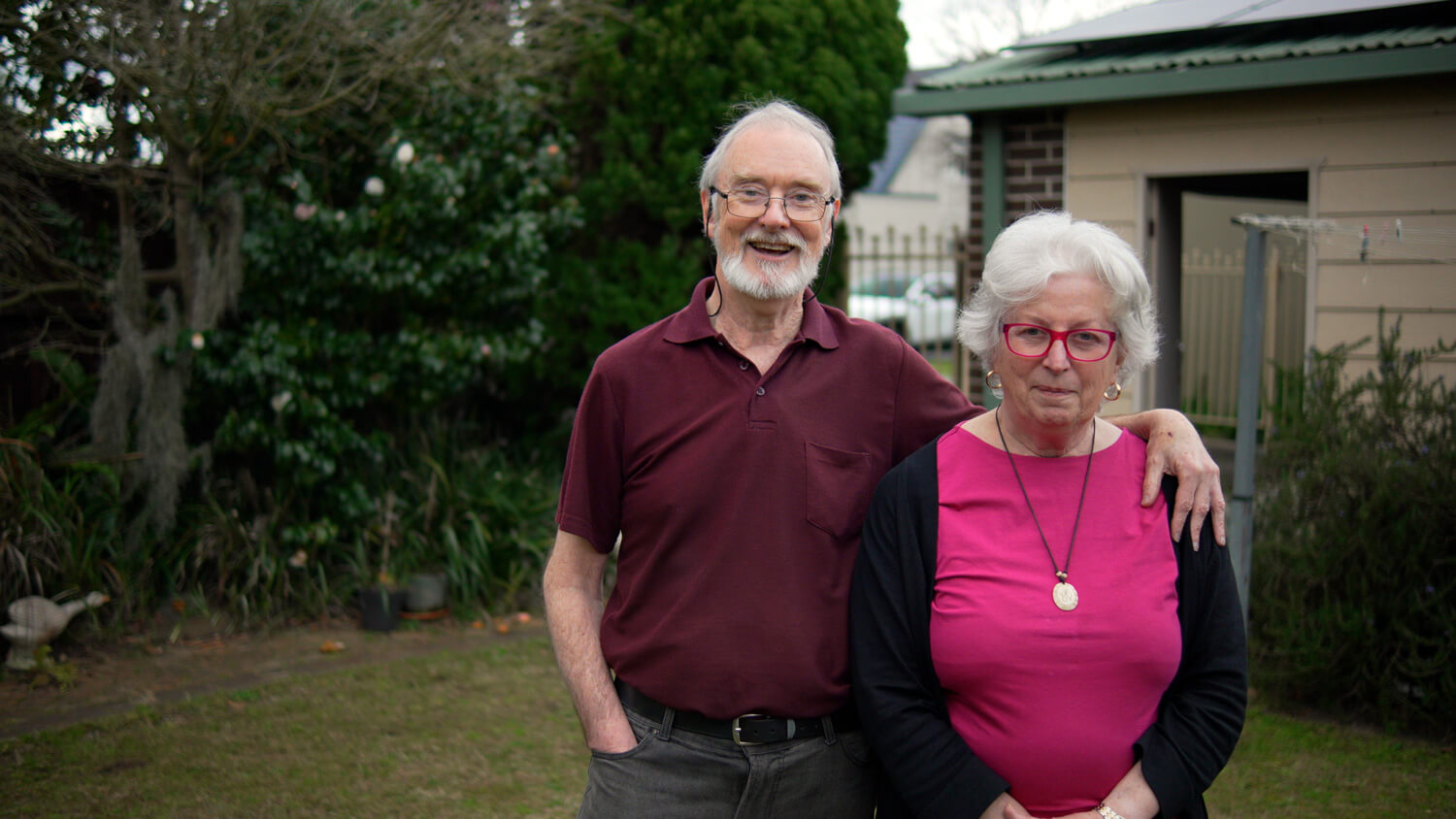 Two people standing in front of their home, smiling to the camera