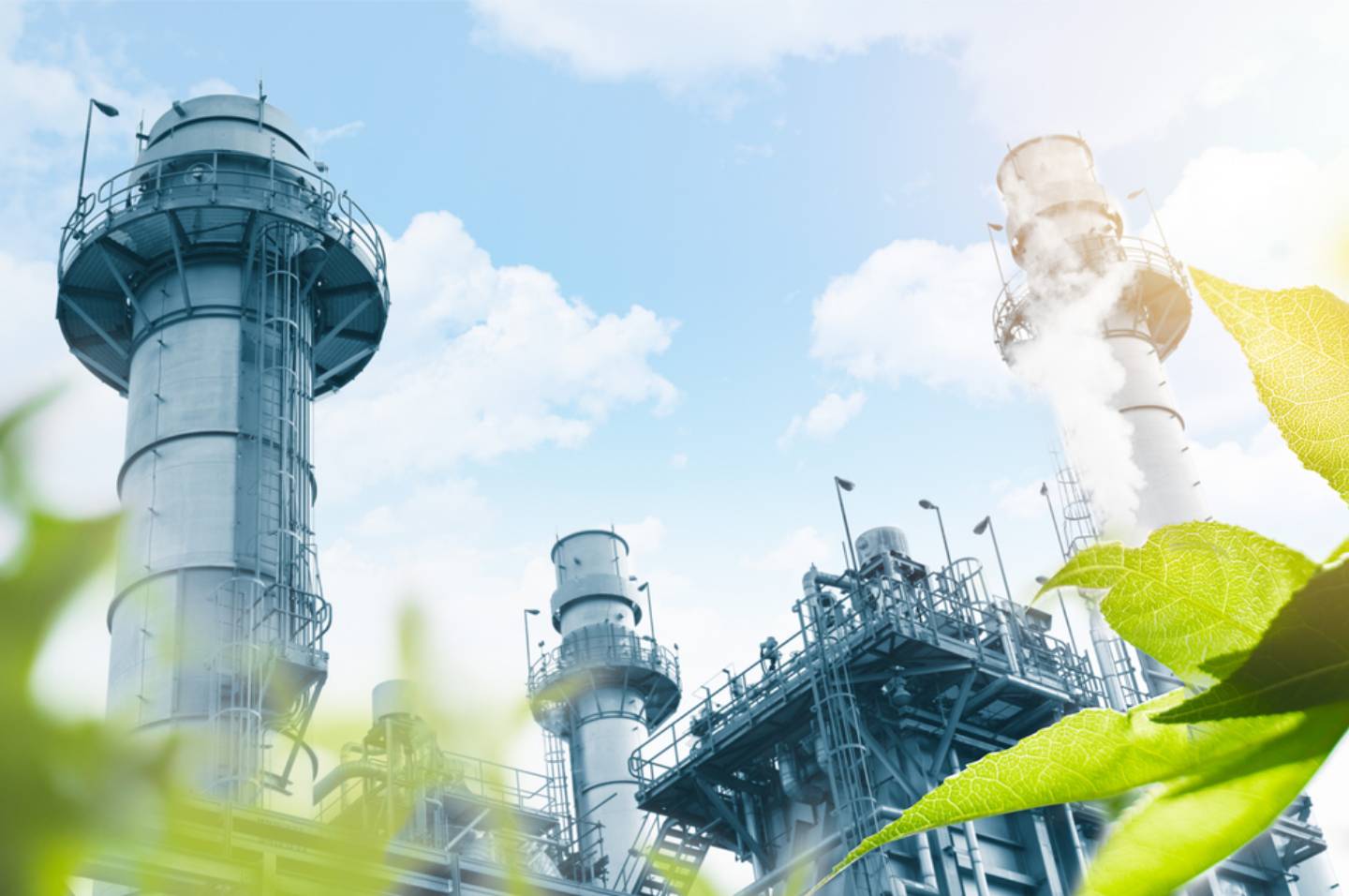 Vibrant green trees in front of factory chimney stacks