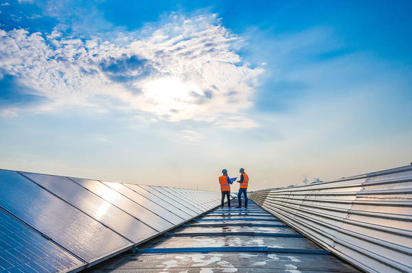 Two workers on a roof with solar panels reflecting clouds
