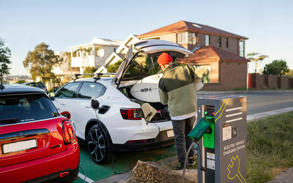 Person putting surfboard into electric vehicle parked at outdoor pedestal charger