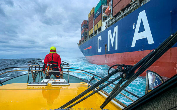 Ship carrying containers, person on smaller boat