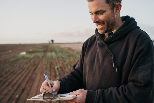 Man in field writing on clipboard