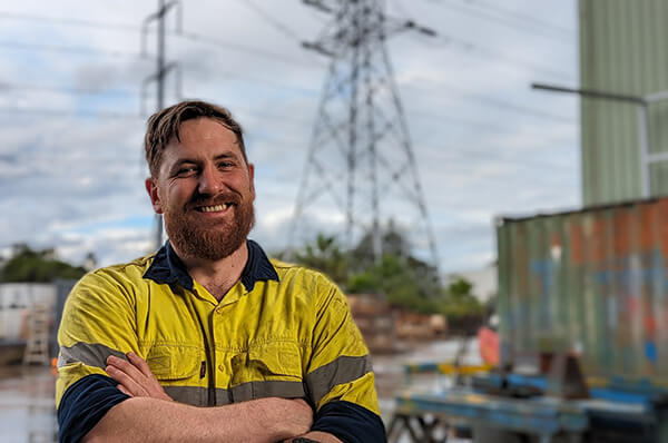 Person in high vis smiling, electricity transmission tower in background